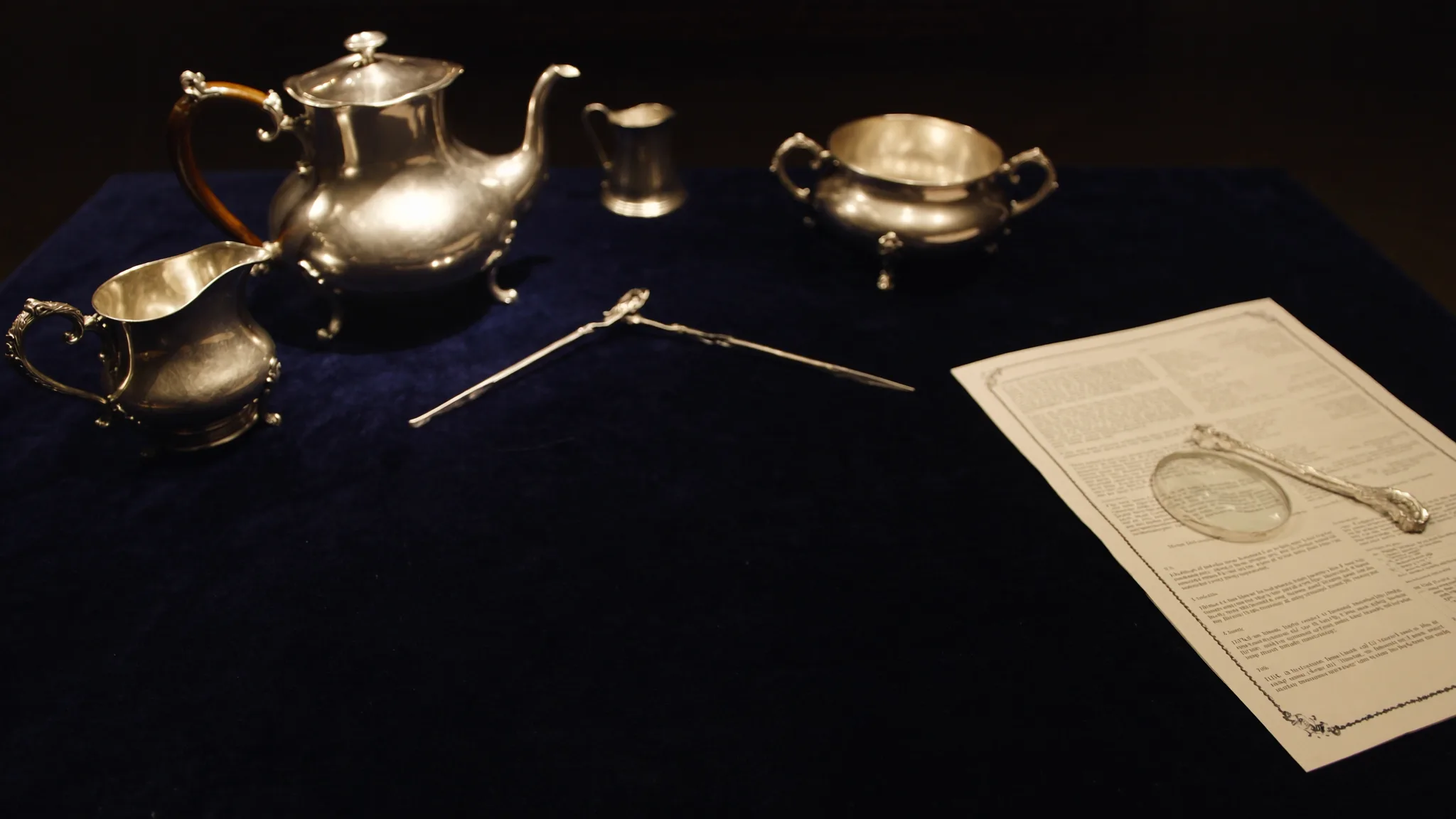 Georgian silver tea service arranged on dark blue velvet beside a magnifying loupe and an open auction catalogue — an editorial composition representing how sets and collections are valued for probate.