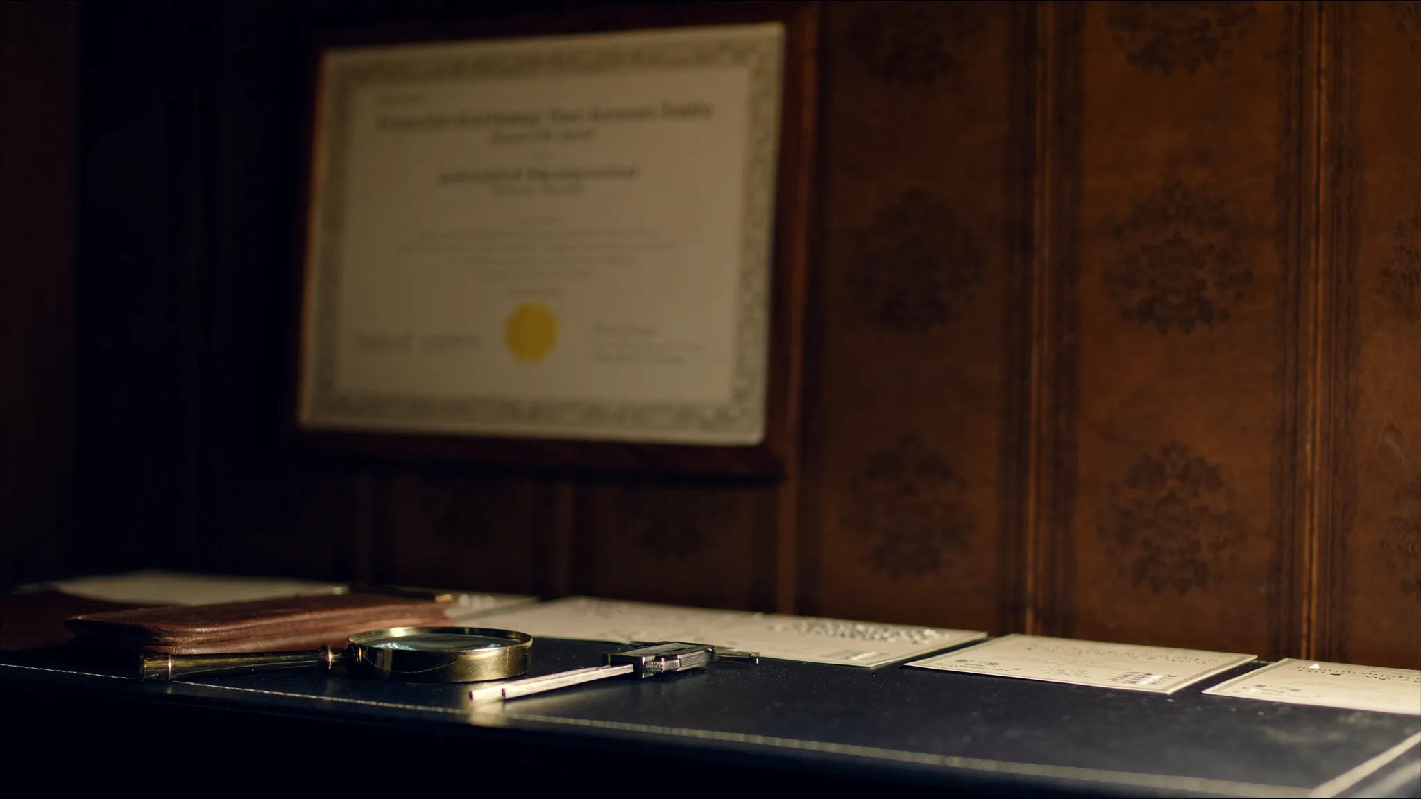 Jeweller's loupe and calipers arranged on dark leather beside a framed professional certificate — an editorial composition representing probate valuer qualifications.